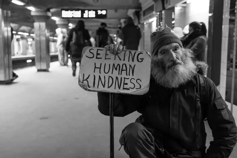 homeless man holding a banner saying he is seeking kindness