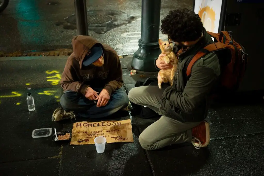 guy holding a ginger cat speaking to a homeless man on the street