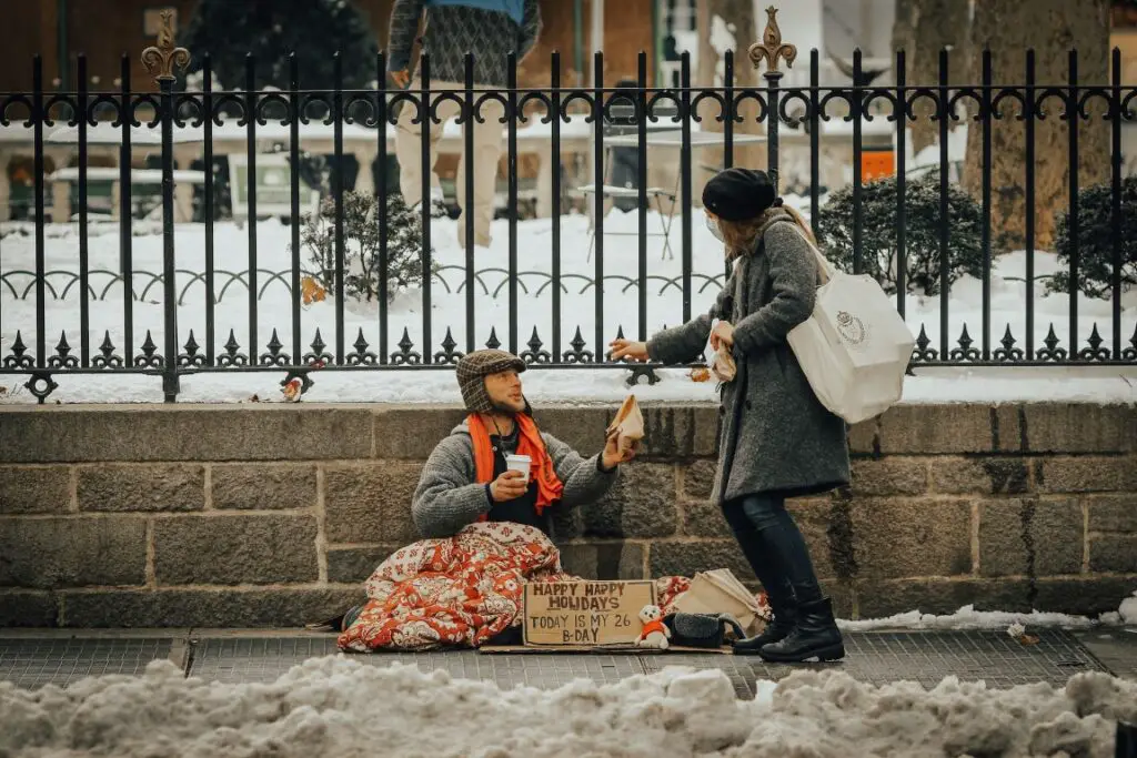 Young lady giving a sandwich to a homeless man sitting by the road